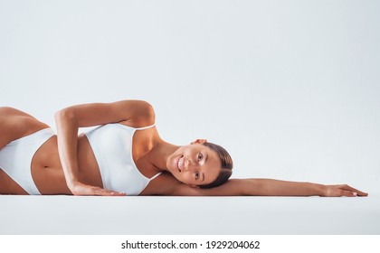 Lying down on the floor. Beautiful woman with slim body in underwear is in the studio.