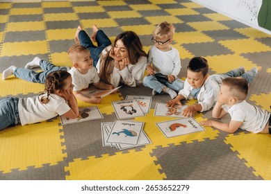 Lying down on floor, learning new words. Children in kindergarten with their teacher.