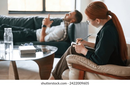 Lying down on the sofa. Man is on the therapy session with female psychologist.