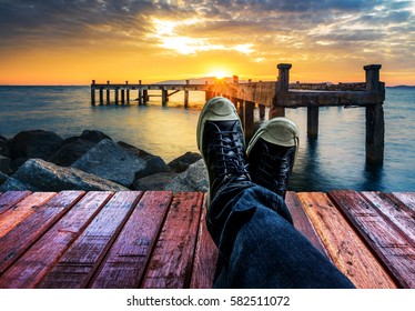 Lying on the pier stretching legs in the shoes with sunrise over the sea, Thailand