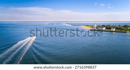 Lynde Point Lighthouse (Inner Light) and its adjacent keeper's house are captured in this drone aerial photograph during a gorgeous summer sunset in Old Saybrook, Connecticut, New England, USA. The historic white, octagonal tower stands on the shore, with the private homes of the affluent Fenwick section lining the nearby beach, all bathed in the warm light of the sun setting over the Connecticut River mouth.