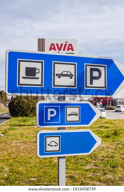 LYON, FRANCE - FEBRUARY 26, 2019: road signs\
to cafe and parking at AVIA gas service station in Lyon, France on\
blue sky background