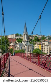Lyon, France - May 11, 2022 : People crossing a red bridge and the old city of Lyon in the background 