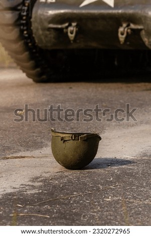 An M1 american infantry   helmet from the Second World War lies on the ground. In the background Sherman tank.