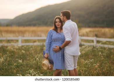 Ma and his pregnant wife stand in field near the farm and hug each other - Shutterstock ID 1200185680