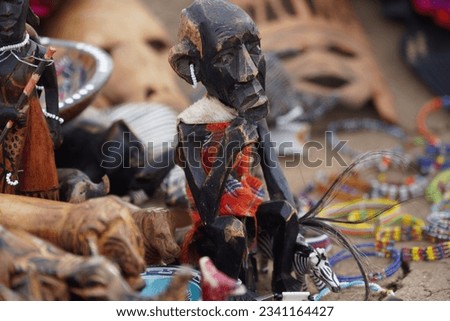 A Maasai figure carved from wood wearing a traditional checkered fabric dress and beaded earrings.