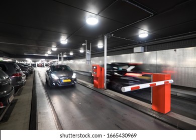 MAASTRICHT, NETHERLANDS - MARCH 02 2020: Underground Parking Garage With Parked Cars And Cars That Drive In And Out. The Barrier Is Closed