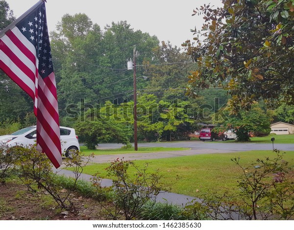 Mableton, Georgia, USA - July 5, 2019: American flag\
and cars parked at driveway next to rural houses at Mableton in a\
rainy day.