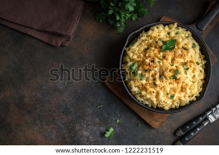 Mac and cheese, american style macaroni pasta with cheesy sauce and crunchy breadcrumbs topping on dark rustic table, copy space top view