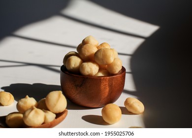 Macadamia nuts in wooden bowl on white table with sunlight and shadow. Macadamia nuts are a source of protein packed with healthy vitamins.