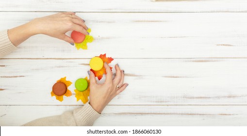 Macaron cakes and female hand with manicure on a white wooden background. Autumn leaves lie. - Powered by Shutterstock