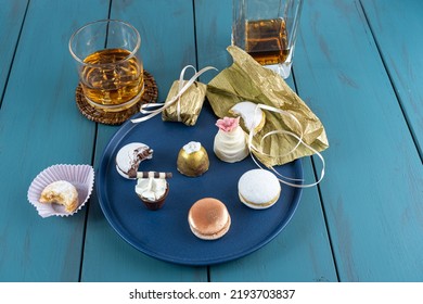 Macaron Next To Small Chocolate Glass With Whipped Cream, Walnut Cameo, Truffle, Whiskey Bottle And Glass.