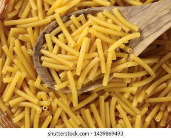 Macaroni, raw pasta in wooden food basket with spoon, top view