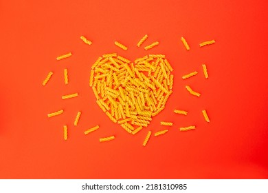 Macaroni uncooked short dry pasta heart shaped layout. Valentine's day symbol, valentine on red background. Love cooking and food concept.