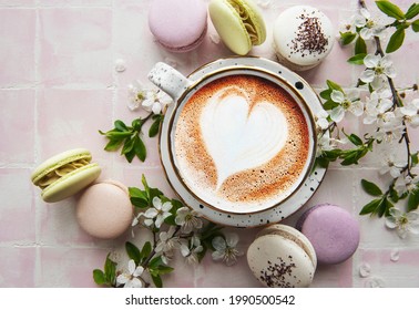 Macaroons with a cup of coffee and a branch of white flowers on a pink tile background. French dessert and flowers 