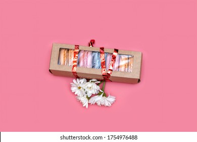 macaroons in a thin closed box decorated with a ribbon and flowers on a pink background