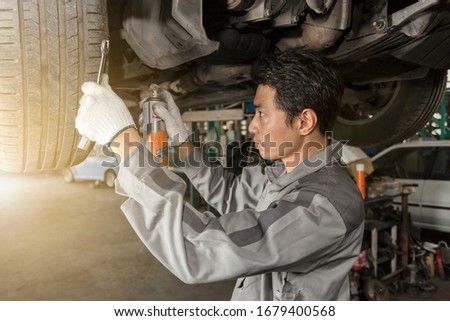 Machanic technician checking and spraying engine oil into a spare parts of wheel under the car to repair and maintenance on hydraulic lift at automobile repair shop.