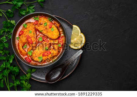 Macher Jhol in black bowl on dark slate table top. Indian cuisine Bengali Fish Curry. Asian food and meal. Top view. Copy space