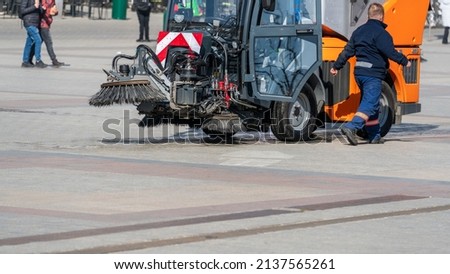 The machine cleans the city square. The driver of a communal vehicle for cleaning roads and sidewalks on city streets got out of the cab