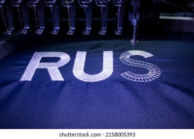 Machine embroidery of the inscription Russia on a blue T-shirt with white thread. Selective focus.