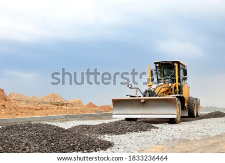 Сonstruction machine Motor Grader at a construction site level the ground and gravel stones for the construction of a new asphalt road. Road construction equipment. Roadworks concept