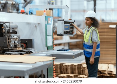 Machine operators work in a large paper factory and check stock of cardboard boxes.