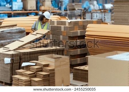 Machine operators work in a large paper factory and check stock of cardboard boxes.