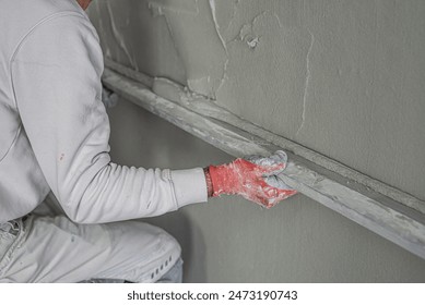 Machine plastering. Applying gypsum plaster by mechanized method on a wall. A worker hand removes excess plaster with leveler.