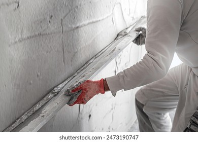 Machine plastering. Applying gypsum plaster by mechanized method on a wall. A worker hand removes excess plaster with leveler.