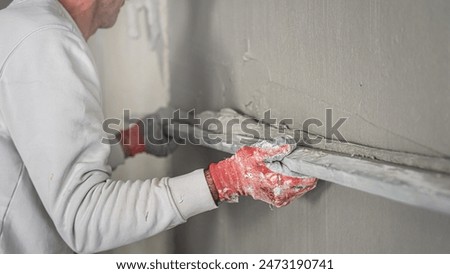 Machine plastering. Applying gypsum plaster by mechanized method on a wall. A worker hand removes excess plaster with leveler.