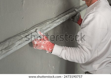 Machine plastering. Applying gypsum plaster by mechanized method on a wall. A worker hand removes excess plaster with leveler.