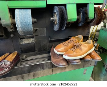 A Machine Used To Fix And Shine Shoes At A Shoe Repair Shop. There Is A Sanding Machine, Buffers, And Different Men's Shoes Lined Up On The Counter.