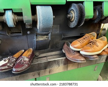 A Machine Used To Fix And Shine Shoes At A Shoe Repair Shop. There Is A Sanding Machine, Buffers, And Different Men's Shoes Lined Up On The Counter.