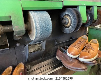 A Machine Used To Fix And Shine Shoes At A Shoe Repair Shop. There Is A Sanding Machine, Buffers, And Different Men's Shoes Lined Up On The Counter.