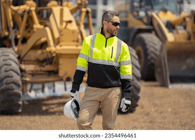 Machinery builder at buildings background. Excavator loader tractor and buider worker. Construction worker with tractor or construction vehicle. Engineer worker in hardhat near digger tractor.