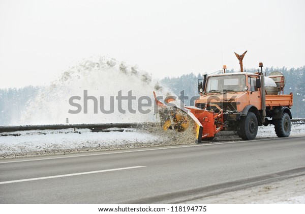 Machinery with snowplough\
cleaning road by removing snow from intercity highway after winter\
blizzard