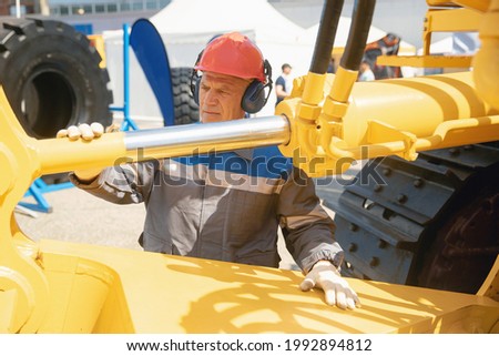 Machinery tractor mechanic checks hydraulic hose tube system equipment on excavator.