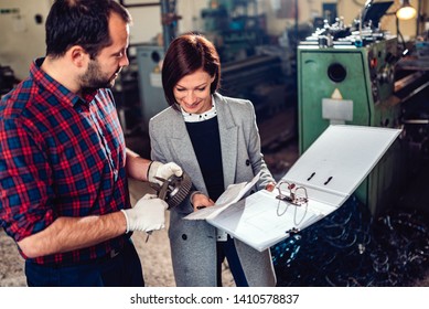 Machinist Standing With Female Engineer And Measuring Cogwheel Diameter With Caliper At Industrial Manufacturing Factory