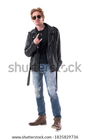 Macho rocker man showing two finger horns or devil hand sign gesture in black leather jacket. Full body isolated on white background.