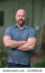 Macho tough guy posing with arms crossed. Man is bald with a full beard