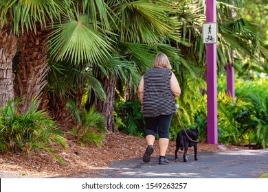 Mackay, Queensland, Australia: 3rd November 2019: Overweight Woman Walking With Dog On A Sunny Morning In The Botanic Gardens