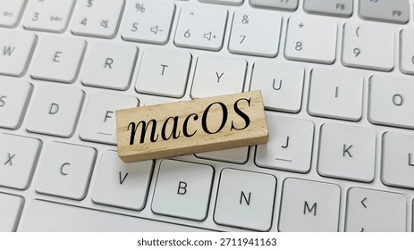 macOS operating system logo on wooden block on white modern keyboard, illustrating software technology, Apple ecosystem, computing, digital platforms, and IT solutions. 