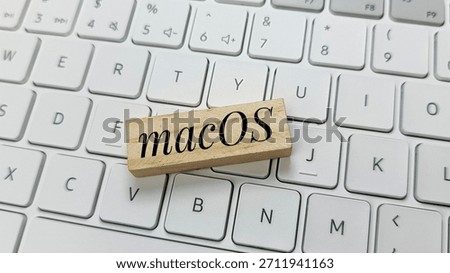 macOS operating system logo on wooden block on white modern keyboard, illustrating software technology, Apple ecosystem, computing, digital platforms, and IT solutions. 