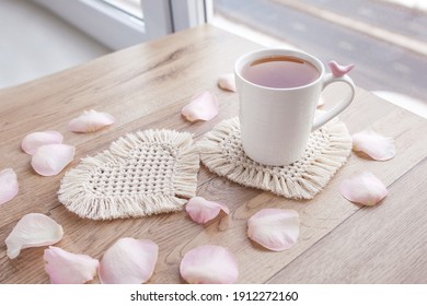 Macrame handmade Hobby.  Tea in a cup on white macrame coaster on wooden table with rose petals.  Food stylist. Eco macrame home decoration. St. Valentine's Day