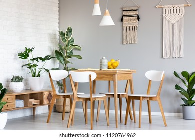 Macrame hanging on gray wall above wooden table and chairs in bright dining room interior with lots of plants. Real photo