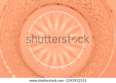 Macro abstract texture background of a round translucent lead crystal glass surface with a starburst design and diamond cuts, in the color of orange
