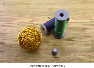 macro ball of gold threads, threads and needle. a thimble on a wooden background