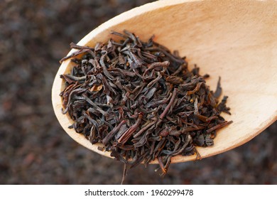 macro of black loose long leaf tea in wooden spoon
