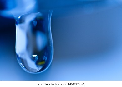 Macro blue water droplet from faucet with variety of reflections, on blue background.