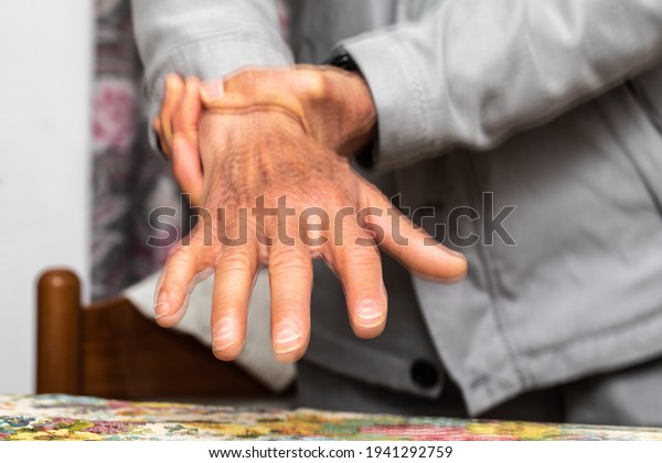 Macro of a caucasian elderly hand with\
tremors. Blurred effect of a double exposure. Concept of\
Parkinson\'s disease patient trying to calm hand\
shaking.